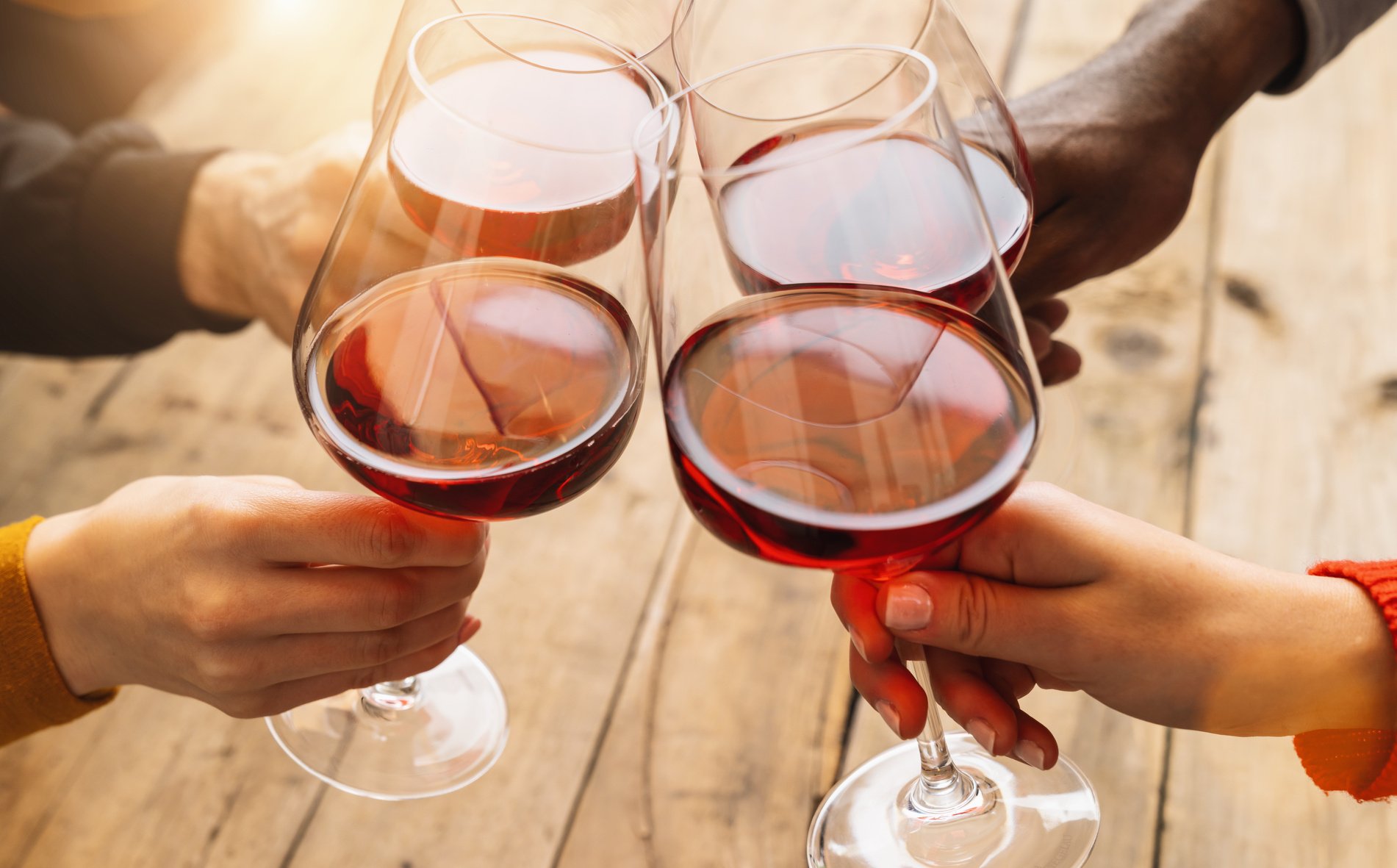 Hands Toasting Red Wine Glass and Friends Having Fun Cheering at